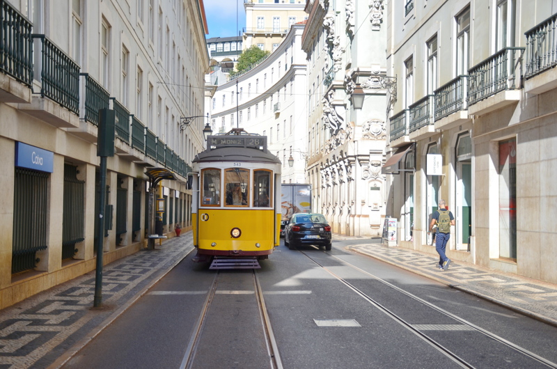 21 - The iconic vintage yellow Tram 28 (Eléctrico 28) navigating a narrow, historic street lined with traditional architecture and tiled sidewalks in Lisbon